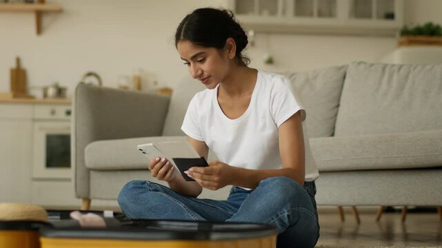 Hindu woman Indian girl Arabian female at home prepare for trip vacation travel using browsing smartphone order fly chat mobile phone booking hotel packing clothes in suitcase holding tickets passport