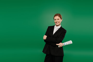 The TV presenter, dressed in stylish black suit, poised to engage the audience before a vivid green backdrop.