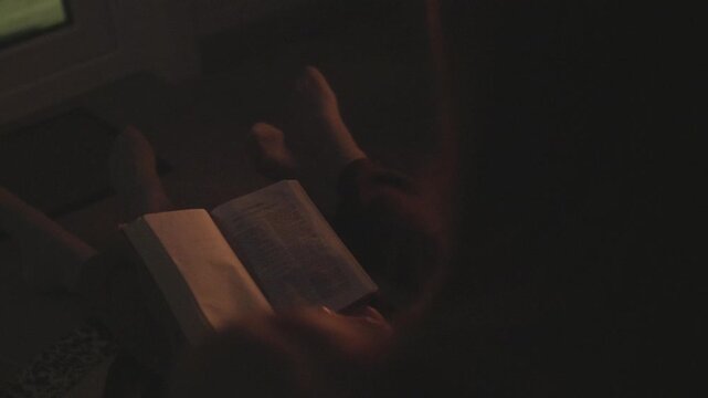 A mom with her son and daughter sitting on the floor next to the sofa and reading a book by the fireplace. Atmosphere of comfort and warmth in the house.