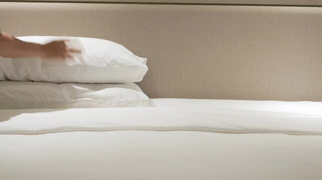 Asian man housekeeping cleaning bed make up arranging blanket,set up pillows and bedding in bedroom after wake up in the morning time, cleaning bedroom in resort hotel ready for guest check in