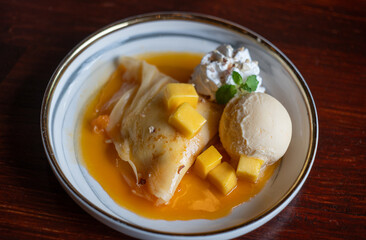 a dish of mango crepe with mango sauce and vanilla ice-cream