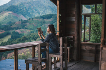 a woman sitting on a wood chair and reading a book in a mountain view