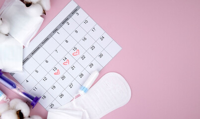 Women's menstrual pads, tampons, female menstruation calendar and alarm clock on a pink background.
