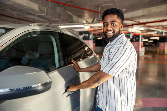 Smiling young african american man opening door on his car at public garage.