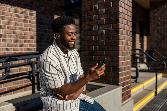 Happy african american man having conference call at train station and waiting for train departure.
