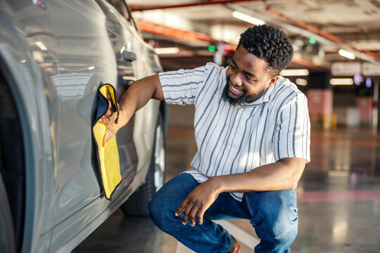 Happy black man is polishing his car with microfiber cloth.