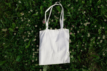 White cotton or mesh bag on green grass with clover flowers background. Zero waste, no plastic, eco friendly shopping, recycling concept. Blank mockup shopper, place for text. copy space flat lay