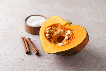 Cut raw orange pumpkin with seeds, cinnamon and sugar on a beige textured stone background. Preparing pumpkin for baking