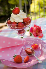 Summery al fresco still life of strawberries and cream in a glass  on a table in a garden