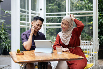 Young couple is deeply engaged in discussion while using a tablet at an outdoor cafe. The setting is casual and the atmosphere is collaborative, indicating a thoughtful brainstorming session.