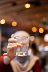 A person holds a glass of fresh water in a cozy cafe setting with blurred background. The warm, ambient lighting creates a relaxing and inviting atmosphere for hydration and reflection.