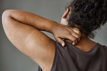 Close up of unrecognizable African American woman scratching back and neck in minimal grey studio,...