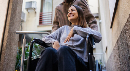 Young woman in wheelchair leaving building with friend's help