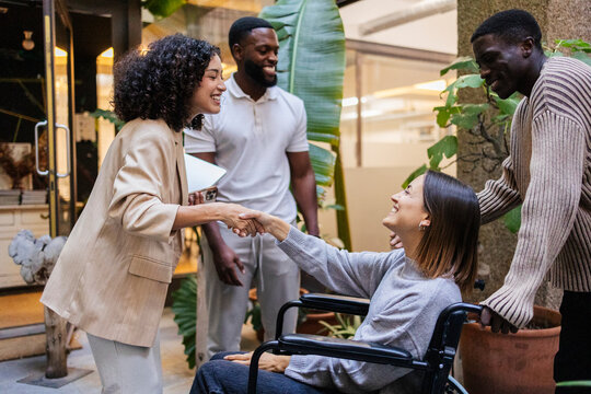 Managers shaking hands with a young woman in a wheelchair in a coworking space