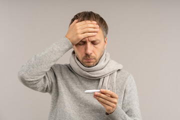 Man with flu respiratory symptoms suffering from fever touches hot forehead holds thermometer...