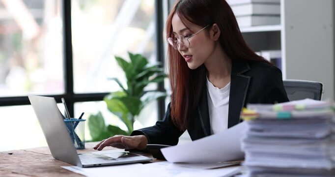 Asian Business woman using calculator and laptop for doing math finance on an office desk, tax, report, accounting, statistics, and analytical research concept
