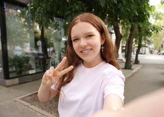 Fototapeta premium Beautiful teenage girl taking selfie on city street