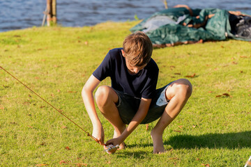 young son boy setting up a large, beige camping tent on a grassy area near a lake work together shared camping experience feelings of relaxation for a camping or outdoor adventure concept.