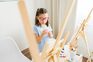 Young girl getting ready to paint next to an easel in an elementary school art class