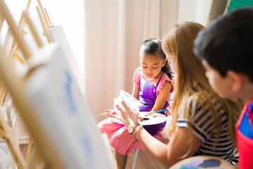Art teacher assisting a young girl in choosing colors from a palette, nurturing creativity and...