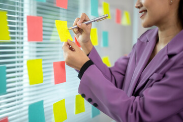 A woman is writing on a wall with colorful sticky notes