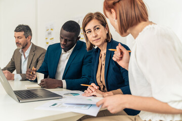 Diverse business team analyzing financial data mature female executive leading multigenerational...