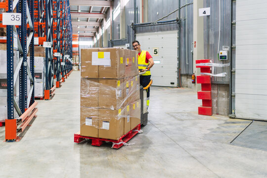 Warehouse worker transporting goods on pallet jack in logistics center