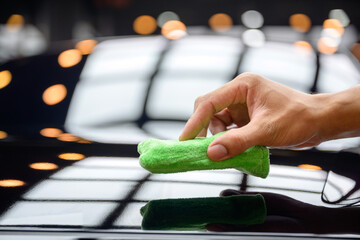 A close-up of a green microfiber cloth being used to manually apply ceramic coating, which improves shine and protects the paint on a black car surface. Perfect for images of auto maintenance