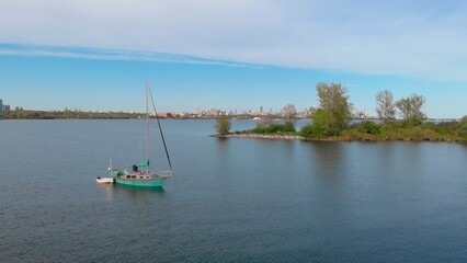 Fototapeta premium Drone view of yacht anchored on calm lake Ontario waters with Toronto skyline in background. Scene captures peaceful blend of nature and city, showcasing freedom and serenity amidst urban energy.