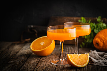 Fresh organic orange drink or cocktail in a glass cup with an orange slice on a wooden table.