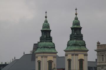 Twin church towers with green domes rise against a cloudy sky, showcasing intricate architecture in...