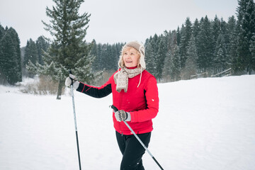 acrive senior woman wearing red winter jacket outdoots portrarit - skiing in forest