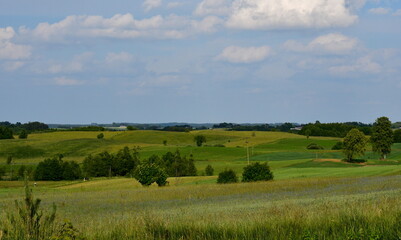 A view from the top of a tall hill or mountain showing various fields, meadows, and pasturelands surrounded with forests, moors, small villages and farmlands spotted on a sunny summer day in Poland