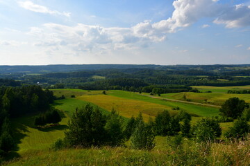 A view from the top of a tall hill or mountain showing various fields, meadows, and pasturelands surrounded with forests, moors, small villages and farmlands spotted on a sunny summer day in Poland