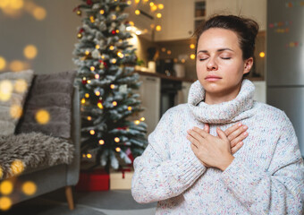 Woman in a warm knit sweater meditating and practicing breathing exercises at home during Christmas...