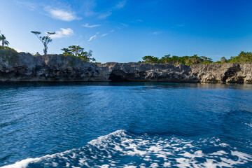 A serene body of water reflects the clear blue sky, while rugged cliffs and scattered trees line...