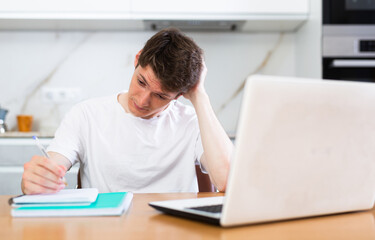 Upset man with laptop and utility bills in kitchen