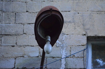 A lamp with a bulb is hanging from a brick wall. The lamp is old and rusted, giving the image a somewhat eerie and abandoned feel.