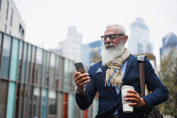 Business senior man using mobile phone and drinking coffee with financial city in background - Job, fashion and technology concept - Focus on face