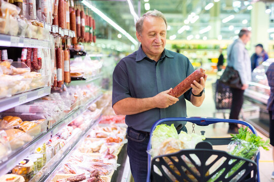 Elderly man chooses sausage in supermarket