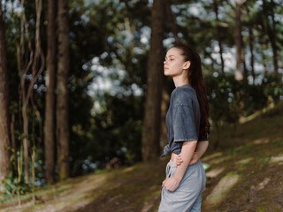 Thoughtful young woman standing in a forest, wearing casual gray outfit, lost in contemplation amidst trees, nature, and tranquility vibe