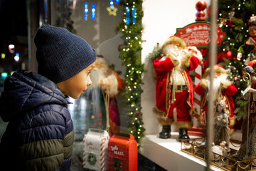 Child looking at festive toy display in Christmas shop window for holiday magic Happy New Year. 