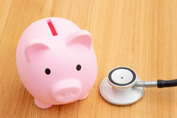 Healthcare costs with a pink piggy bank and a stethoscope on a desk