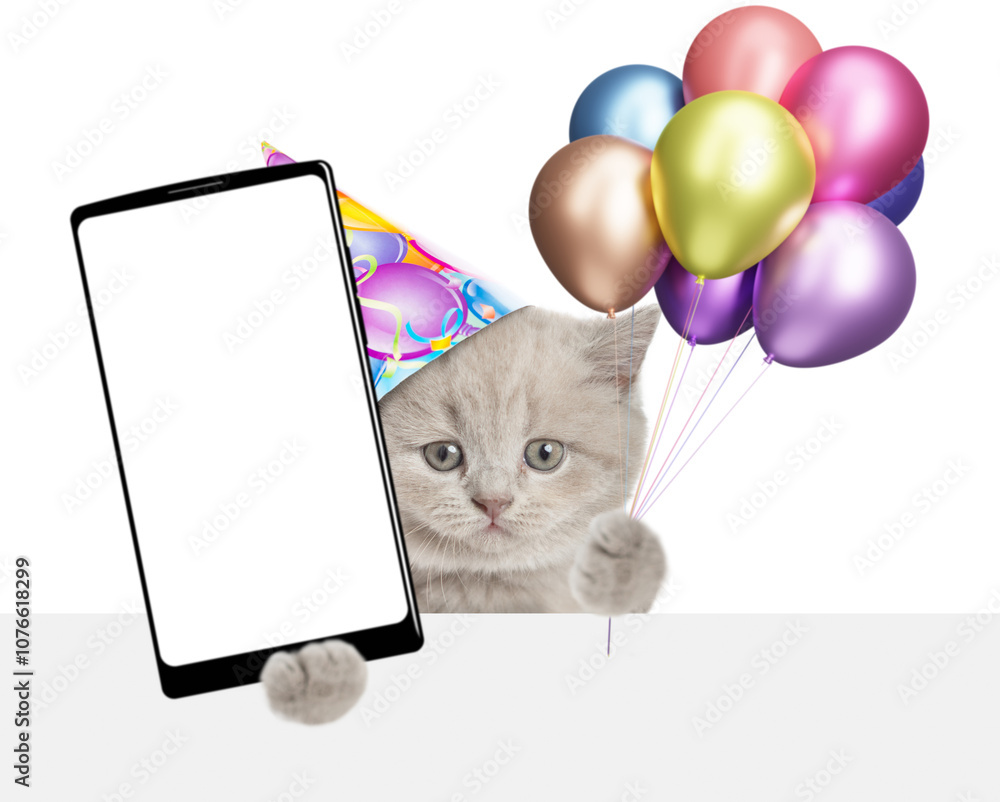 Poster Cute tiny kitten wearing party cap holding balloons and showing big smartphone with blank screen above empty white banner. Empty space for text. isolated on white background