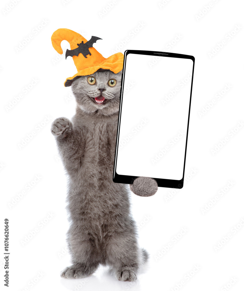 Aufkleber surprised cat wearing hat for halloween holds and shows smartphone with white blank screen in it paw