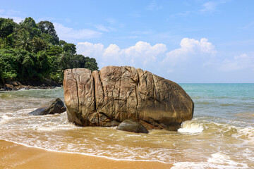Empty tropical beach with big stone, view to yellow sand and blue sea. Background for travel and...