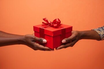 Two black hands exchanging a red gift box against an peach background during a celebration or special occasion