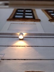 A warm light illuminates a wooden wall and windows at dusk, creating a cozy atmosphere in an urban environment