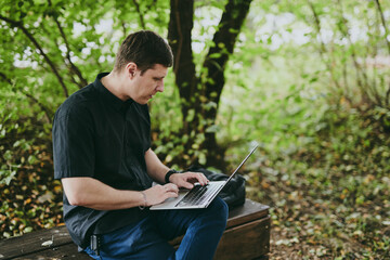 Portrait of young freelance programmer man working with laptop in forest park, software developer, IT technologies