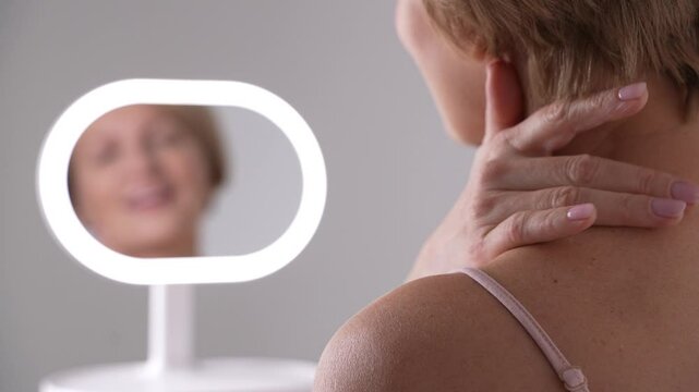 A mature woman tenderly touches her neck and shoulders, celebrating the beauty of graceful aging and the importance of selfcare routines